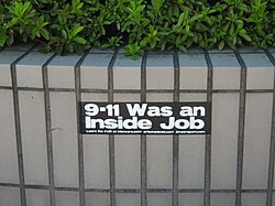 A photo of a black, rectangular sticker that falsely claims that "9/11 was an inside job" in big white text, under the big text was a suggestion to go to three conspiracy theory sites.